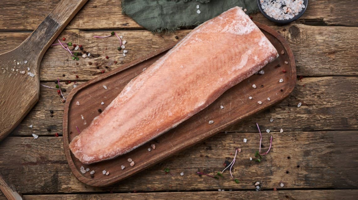 A salmon fillet on a wooden board with salt and herbs