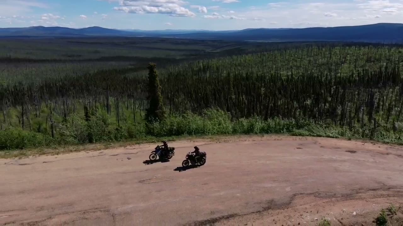 Two motorcycles on a dirt road above a wide northern forest